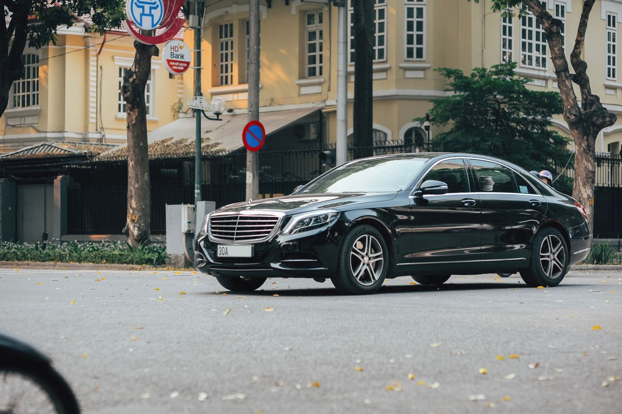 services-01 A sleek black sedan navigates an urban street lined with historic buildings and lush trees.