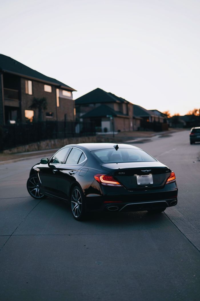 who-we-are A sleek black luxury sedan parked on a quiet residential street during twilight.